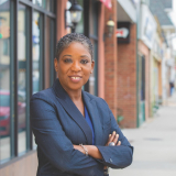 Senator Siela A. Bynoe smiles at the camera while standing outside on the sidewalk of a downtown.