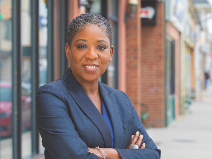 Senator Siela A. Bynoe smiles at the camera while standing outside on the sidewalk of a downtown.