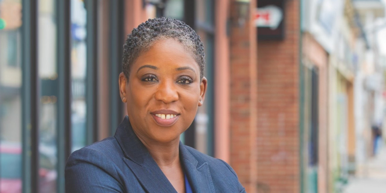 Senator Siela A. Bynoe smiles at the camera while standing outside on the sidewalk of a downtown.