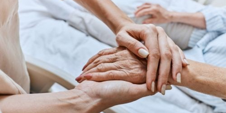 A nurse holds the hand of a hospice patient.