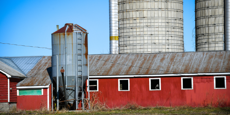 Picture of a red barn with grain silos in the background.