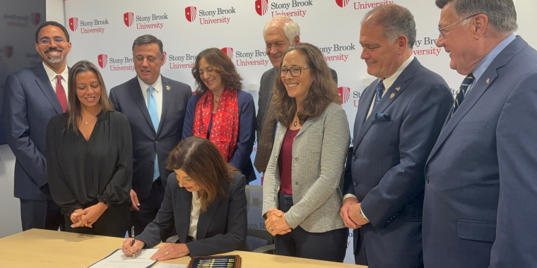 Photo Image of Gov. Kathy Hochul signing a bill sponsored by Sen. Martinez that allows Stony Brook University to develop more on-campus housing.  The governor is surrounded by officials including Sen. Martinez during the signing.