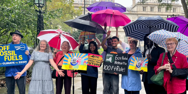 Advocates stand under umbrellas at a press conference