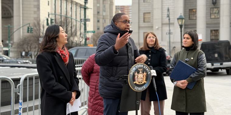 Senator Myrie speaking at a podium in front of the Manhattan Courts